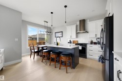 Open-concept kitchen featuring an oversized island with seating, pendant lighting, shaker-style cabinetry, stainless steel range hood, and wood-finish flooring - 