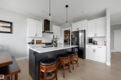 Contemporary kitchen featuring a large central island with seating, white shaker-style cabinetry, stainless steel appliances, and light wood-finish flooring - 