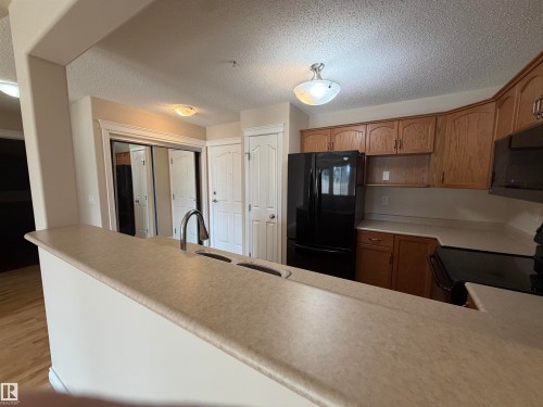 Kitchen featuring a peninsula breakfast bar with integrated sink and chrome faucet, wood-finish cabinetry, black refrigerator, and black range with microwave above - 118 7801 Golf Course Road, Stony Plain, AB 