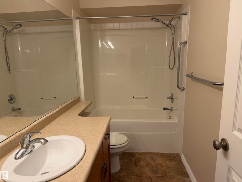 Bathroom featuring an integrated tub and shower unit with chrome fixtures and grab bars, a single vanity with a laminate countertop, an oval undermount sink, and tile-finish flooring - 118 7801 Golf Course Road, Stony Plain, AB 