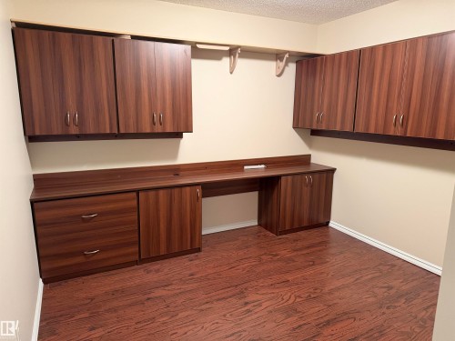 Built-in wood-finish cabinetry and desk surface with integrated power outlets, complemented by wood-finish flooring - 118 7801 Golf Course Road, Stony Plain, AB 