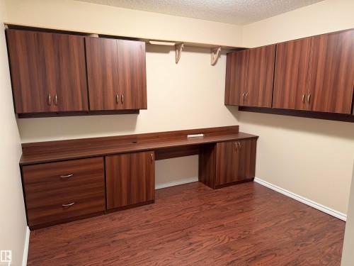 Integrated wood-finish cabinetry and desk system featuring a built-in countertop, multiple upper cabinets, lower cabinets, and drawers - 118 7801 Golf Course Road, Stony Plain, AB 