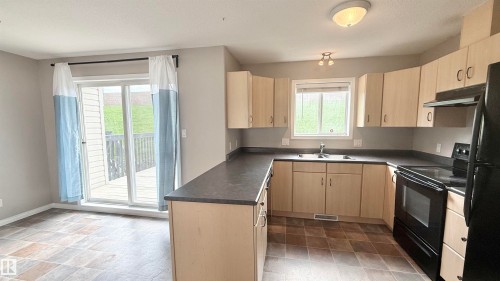 U-shaped kitchen featuring light wood-finish cabinetry, dark countertops, and black appliances - 9 225 Blackburn Drive E, Edmonton, AB 