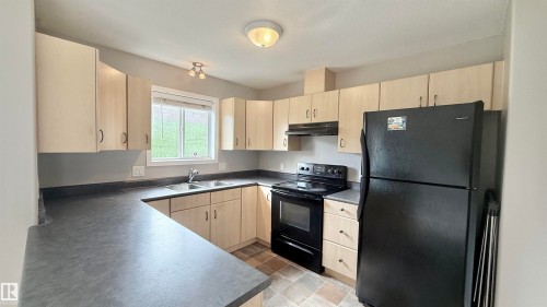 Kitchen featuring light wood-finish cabinetry, dark countertops, and a double basin stainless steel sink - 9 225 Blackburn Drive E, Edmonton, AB 