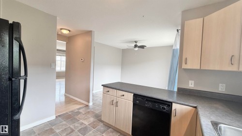 Kitchen featuring light wood-finish cabinetry, dark countertops, and a full-size black dishwasher - 9 225 Blackburn Drive E, Edmonton, AB 