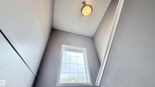 Stairwell featuring a multi-pane window with white trim, a semi-flush mount ceiling fixture, and light gray painted walls - 9 225 Blackburn Drive E, Edmonton, AB 