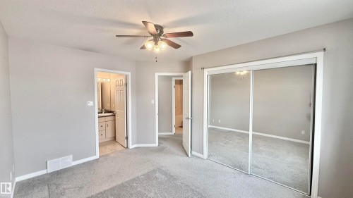 Carpeted interior space featuring a ceiling fan with integrated lighting, mirrored sliding closet doors, and light gray wall paint - 9 225 Blackburn Drive E, Edmonton, AB 