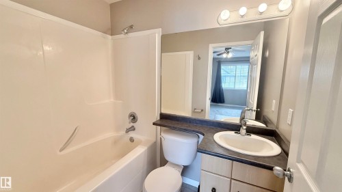 Bathroom featuring a white tub/shower combination, a vanity with a dark countertop and integrated sink, a large wall-mounted mirror, and overhead vanity lighting - 9 225 Blackburn Drive E, Edmonton, AB 