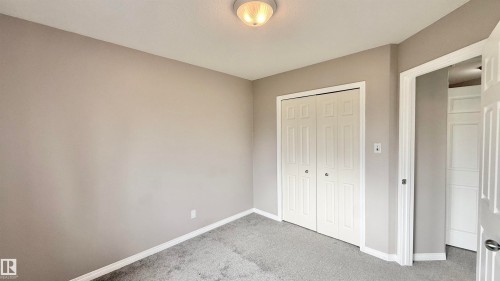 Neutral-toned room featuring a flush-mount ceiling light, paneled bi-fold closet doors, and light gray wall-to-wall carpeting - 9 225 Blackburn Drive E, Edmonton, AB 