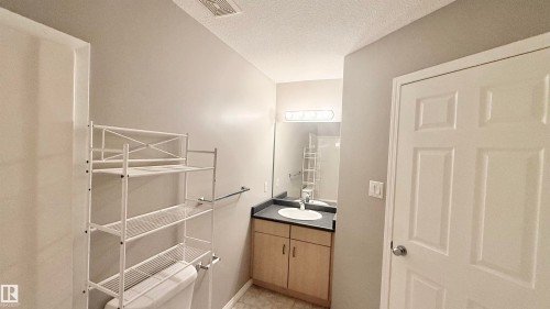 Contemporary bathroom featuring a light wood-finish vanity with a dark countertop and an undermount sink - 9 225 Blackburn Drive E, Edmonton, AB 