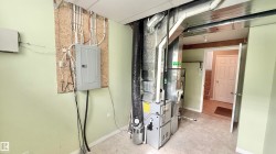 Utility area featuring a furnace system, exposed ductwork, and an electrical panel mounted on an OSB board - 