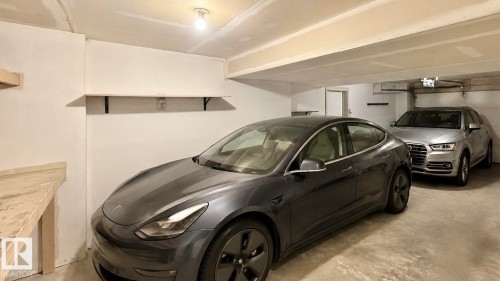 Two-car garage featuring concrete flooring, overhead lighting, an exposed ceiling structure, built-in shelving, and a workbench - 9 225 Blackburn Drive E, Edmonton, AB 