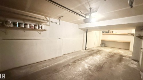 Spacious garage featuring a concrete floor, built-in shelving, and an automatic garage door opener - 9 225 Blackburn Drive E, Edmonton, AB 