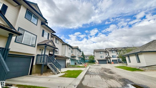 Multi-level residence featuring light-toned siding, dark trim, and a prominent front entrance with covered stairs - 9 225 Blackburn Drive E, Edmonton, AB 