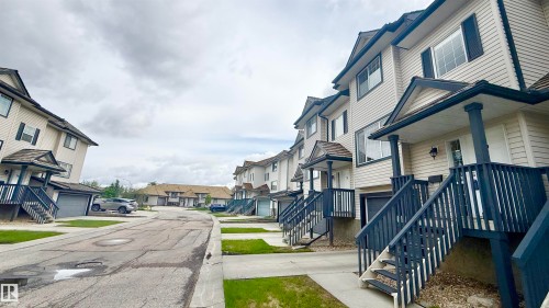 Modern townhome exterior featuring light-colored siding, dark trim, and individual front entrances with covered stoops - 9 225 Blackburn Drive E, Edmonton, AB 