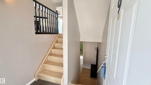 Entryway featuring light wood-finish stairs with dark balusters, gray wall paint, and dark tile flooring - 9 225 Blackburn Drive E, Edmonton, AB 