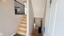 Entryway featuring light wood-finish stairs with dark balusters, gray wall paint, and dark tile flooring - 9 225 Blackburn Drive E, Edmonton, AB 