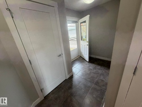Entryway featuring dark square floor tiling, a white paneled door with glass inserts, and white trim - 6821 Evans Wynd, Edmonton, AB 