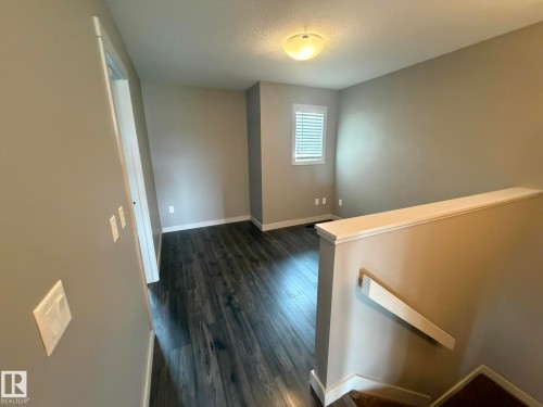 Open landing area featuring dark wood-finish flooring, neutral-toned walls, and a recessed window with blinds - 6821 Evans Wynd, Edmonton, AB 