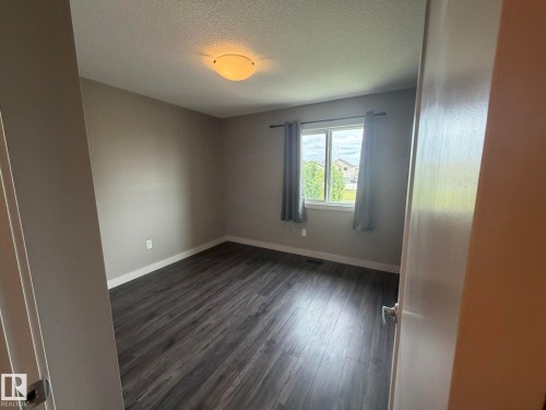 Room featuring dark wood-finish flooring, neutral wall tones, a single window, and a flush-mount ceiling light fixture - 6821 Evans Wynd, Edmonton, AB 