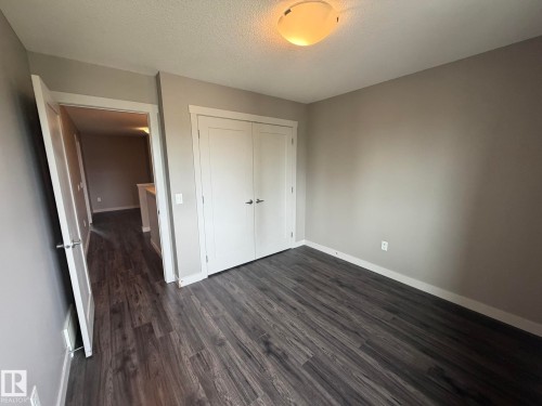 Room featuring wood-finish flooring, neutral wall paint, and a built-in closet with double doors - 6821 Evans Wynd, Edmonton, AB 