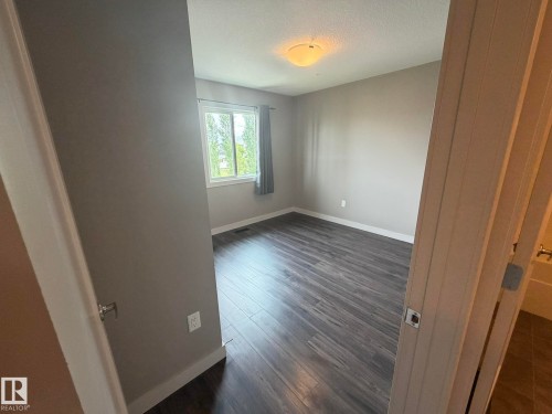 Spacious room featuring wood-finish flooring, a large window, a ceiling-mounted light fixture, and neutral wall paint - 6821 Evans Wynd, Edmonton, AB 