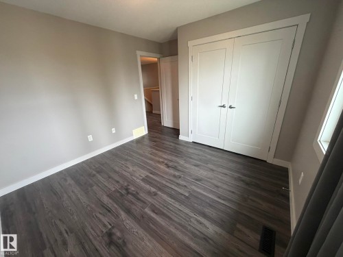 Spacious room featuring wood-finish flooring, light grey walls, white trim, and a white bi-fold closet door - 6821 Evans Wynd, Edmonton, AB 