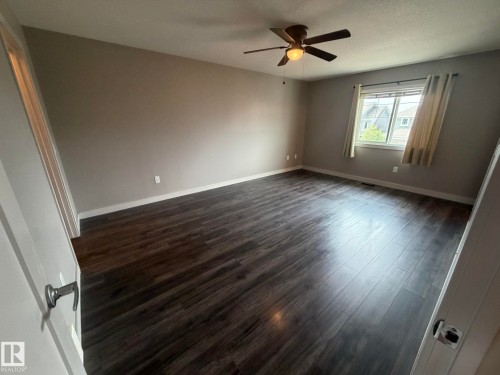 Spacious room featuring dark wood-finish flooring, neutral wall tones, and a ceiling fan with integrated lighting - 6821 Evans Wynd, Edmonton, AB 