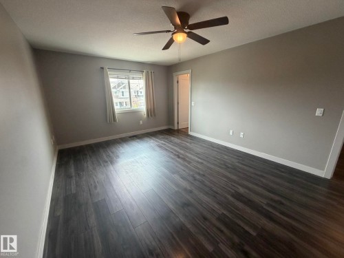 Spacious room featuring wood-finish flooring, neutral gray wall tones, and white trim - 6821 Evans Wynd, Edmonton, AB 