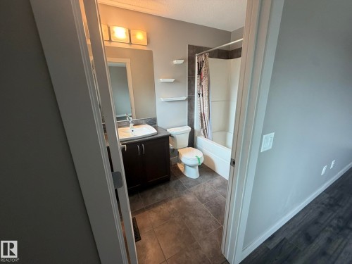 Full bathroom featuring a dark wood-finish vanity with a white vessel sink, a full-width mirror, and overhead lighting - 6821 Evans Wynd, Edmonton, AB 