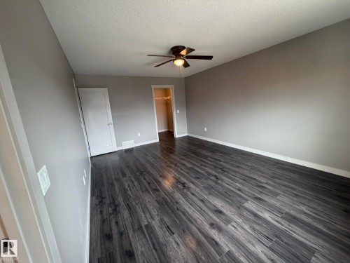 Spacious room featuring dark wood-finish flooring, a ceiling fan with integrated lighting, and neutral gray walls - 6821 Evans Wynd, Edmonton, AB 