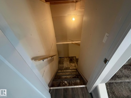 Wood-finish flooring at the landing leading to a partially finished lower level with a wooden handrail - 6821 Evans Wynd, Edmonton, AB 