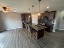 Modern kitchen featuring dark wood cabinetry, stainless steel appliances, a dark tile backsplash, and a spacious island with a double sink and pendant lighting - 6821 Evans Wynd, Edmonton, AB 