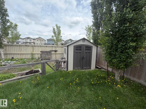 Backyard featuring a compact storage shed with double doors, wood fencing, and established trees - 6821 Evans Wynd, Edmonton, AB 