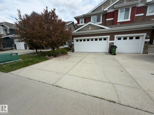 Duplex exterior featuring two white garage doors with window inserts, horizontal siding, and stone accents - 6821 Evans Wynd, Edmonton, AB 