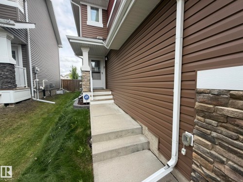 Brown horizontal siding exterior with stone veneer accents, concrete walkway, and white trim details - 6821 Evans Wynd, Edmonton, AB 