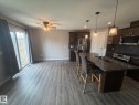 Open-concept kitchen and dining area featuring wood-finish flooring, a kitchen island with stone countertop and integrated double sink, dark wood cabinetry, stainless steel appliances, and sliding patio doors - 6821 Evans Wynd, Edmonton, AB 
