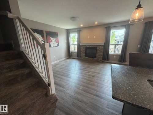 Spacious living area featuring wood-finish flooring, a stone-clad fireplace, and multiple windows - 6821 Evans Wynd, Edmonton, AB 
