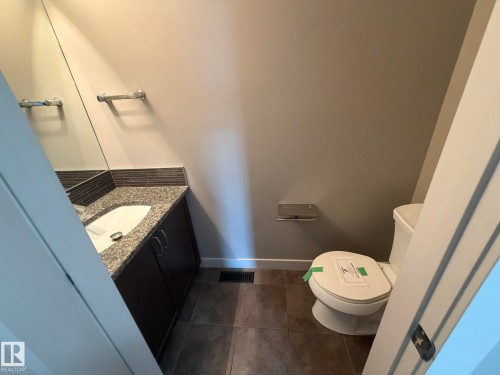 Powder room featuring a dark wood-finish vanity with an integrated sink, granite countertop, and mosaic tile backsplash - 6821 Evans Wynd, Edmonton, AB 