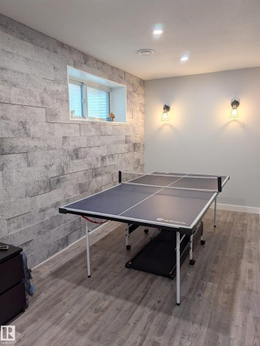 Recreation room featuring a decorative accent wall with stacked stone-look paneling, a recessed window, light wood-finish flooring, and recessed ceiling lights - 9240 224 Street Nw, Edmonton, AB - Indoor Photo Showing Other Room
