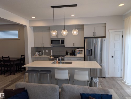 Modern kitchen featuring an island with integrated sink, light grey cabinetry, stainless steel appliances, and wood-finish flooring - 9240 224 Street Nw, Edmonton, AB - Indoor Photo Showing Kitchen With Upgraded Kitchen