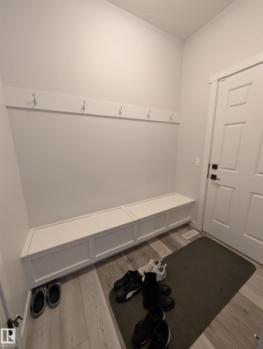 Entryway featuring wood-finish flooring, a built-in white storage bench, a white accent wall with integrated hooks, and a white paneled door with dark hardware - 9240 224 Street Nw, Edmonton, AB - Indoor