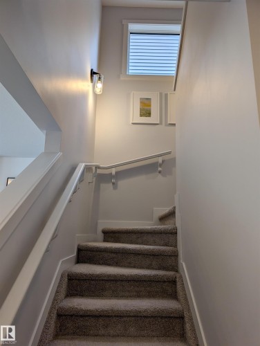 Carpeted staircase featuring a modern wall sconce, white wall paint, and a window with blinds - 9240 224 Street Nw, Edmonton, AB - Indoor Photo Showing Other Room