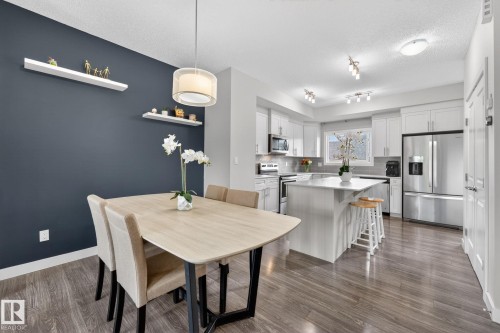 Open-concept kitchen and dining area featuring wood-finish flooring, white cabinetry, stainless steel appliances, and a central island with countertop seating - 165 Robinson Drive, Leduc, AB 