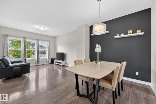 Open-concept living space featuring wood-finish flooring, a contemporary pendant light fixture, and a contrasting accent wall with white floating shelves - 165 Robinson Drive, Leduc, AB 