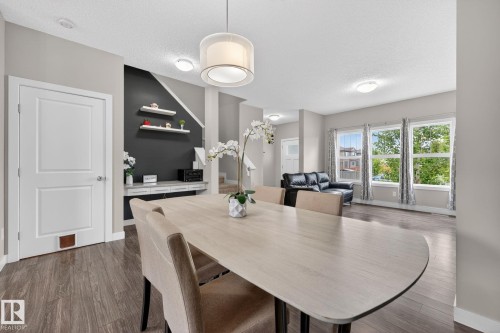 Open-concept dining area featuring wood-finish flooring, a contemporary drum pendant light, and a built-in console with shelving - 165 Robinson Drive, Leduc, AB 