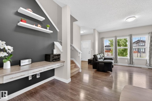 Open-concept living area featuring wood-finish flooring, a built-in desk with integrated drawers, and a painted accent wall - 165 Robinson Drive, Leduc, AB 