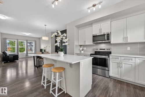 Modern kitchen featuring an island with seating, stainless steel appliances, light gray cabinetry, and a subway tile backsplash - 165 Robinson Drive, Leduc, AB 