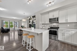Modern kitchen featuring an island with seating, stainless steel appliances, light gray cabinetry, and a subway tile backsplash - 