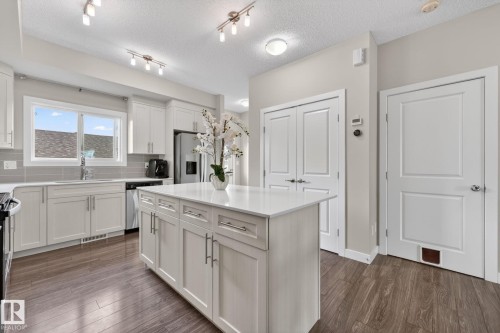 Kitchen featuring wood-finish flooring, a central island with white cabinetry, white countertops, stainless steel appliances, and a gray tile backsplash - 165 Robinson Drive, Leduc, AB 